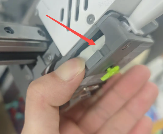 SPARKX i7 extruder flip-down latch — hand pressing the green tab to release